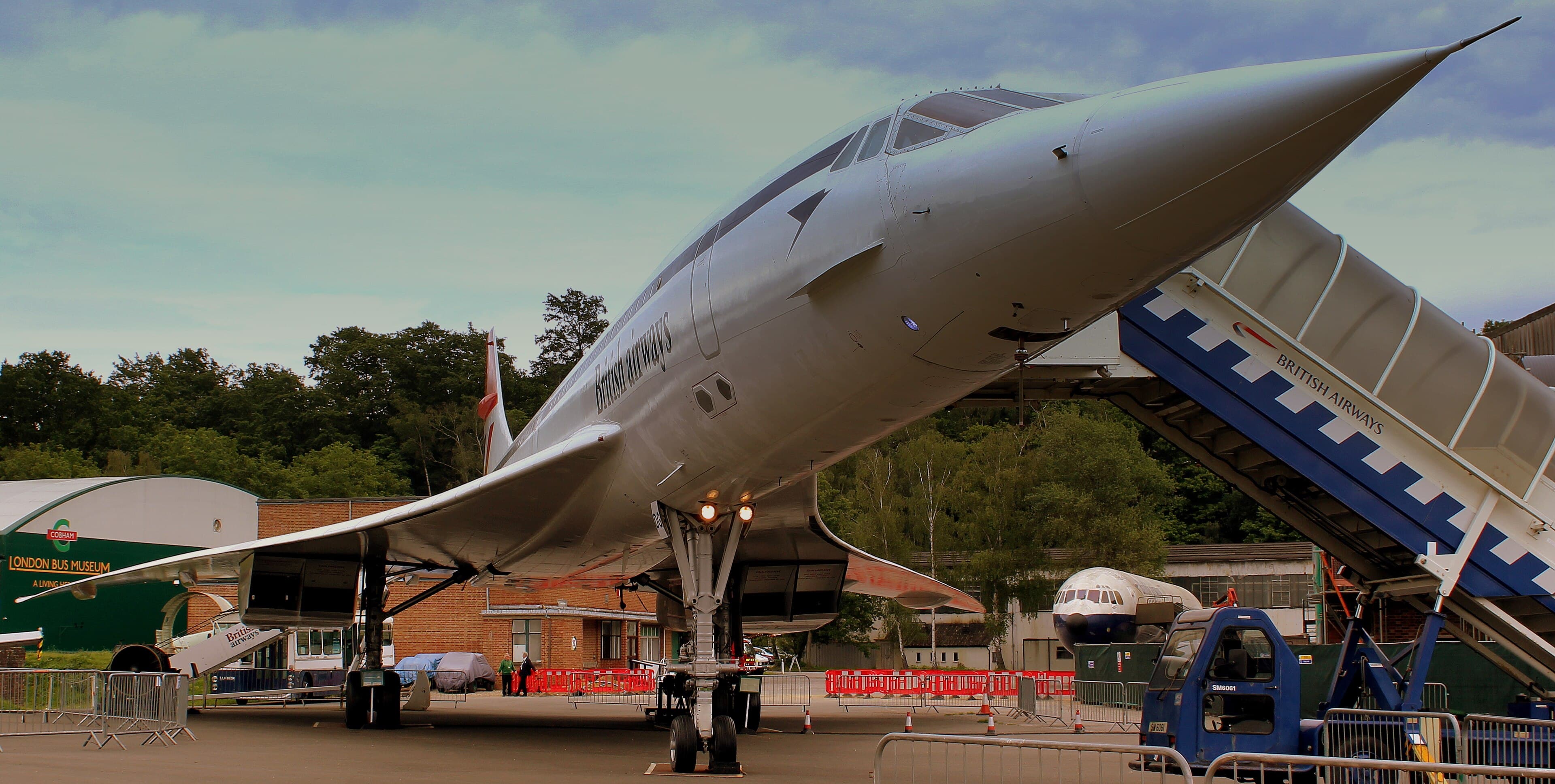 Low view of British Airways Concorde on display at Brooklands Museum, with boarding steps and London Bus Museum building behind